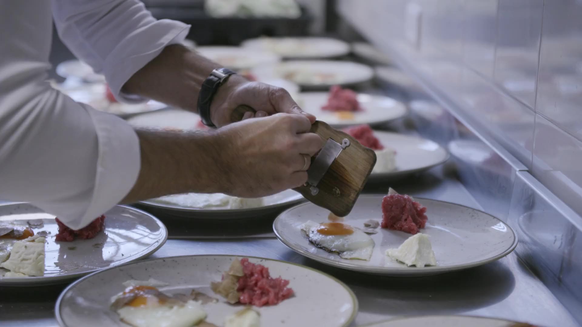 A chef's hands finishing plated dishes along the pass in a professional kitchen