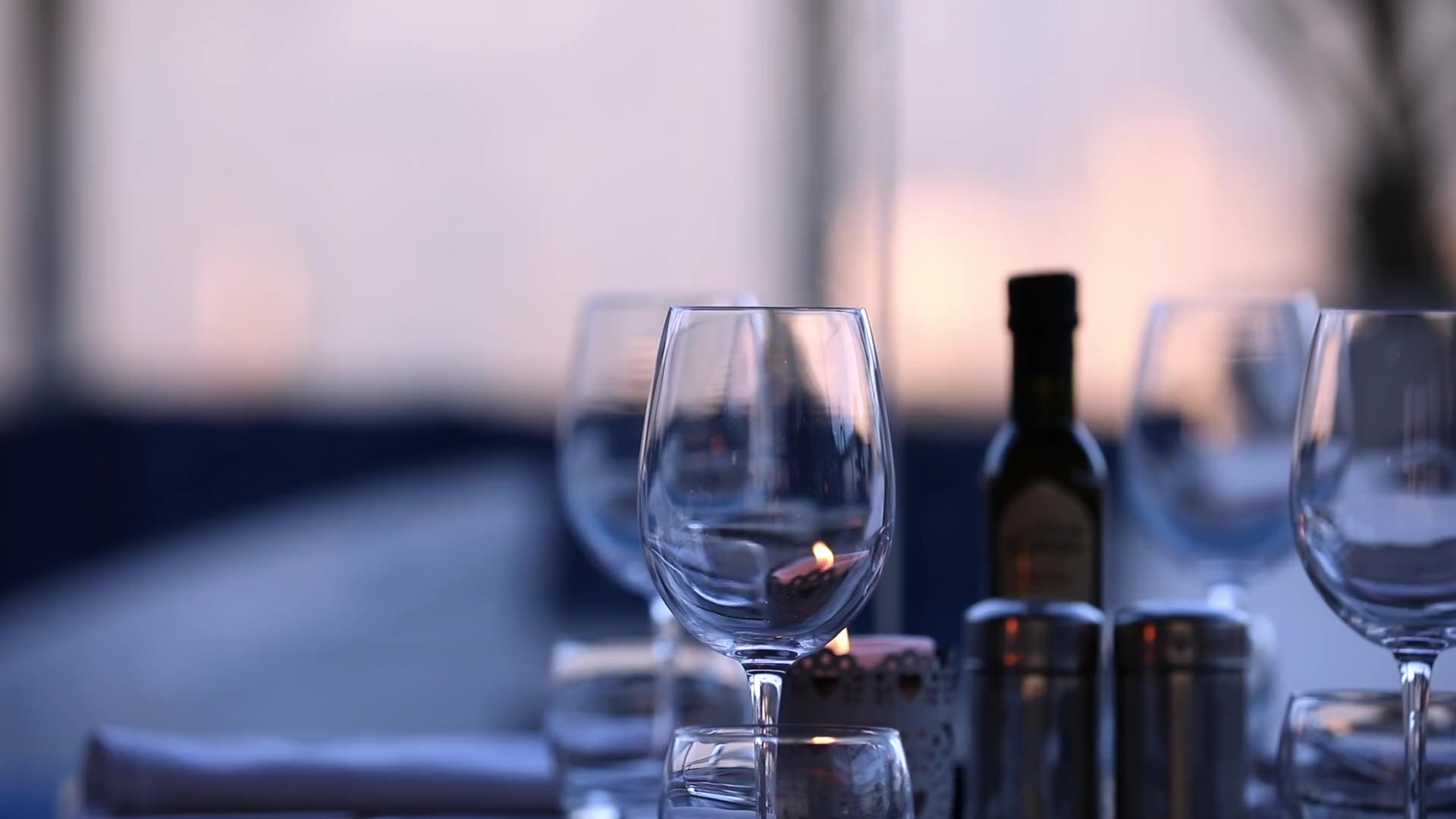 Wine glasses and a candle on a restaurant table at dusk