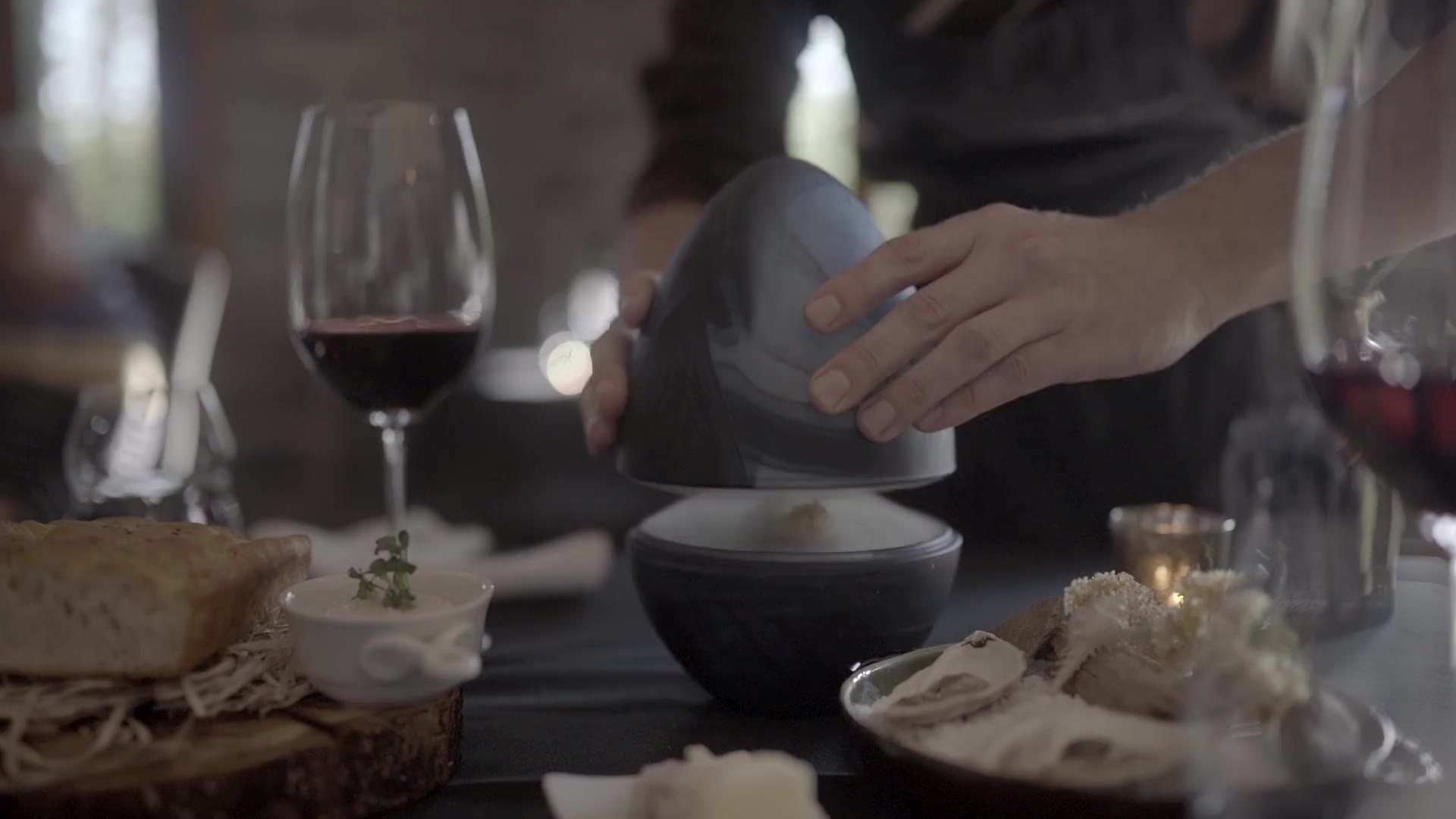 A server lifts a cloche from a dish at a candle-lit table
